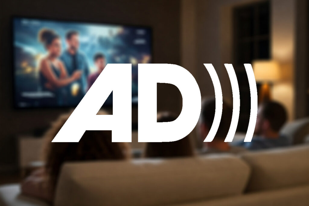 People sitting on a sofa watching television in a dark living room with a table lamp on. The symbol of audio description (AD) appears over the photograph, which is blurred