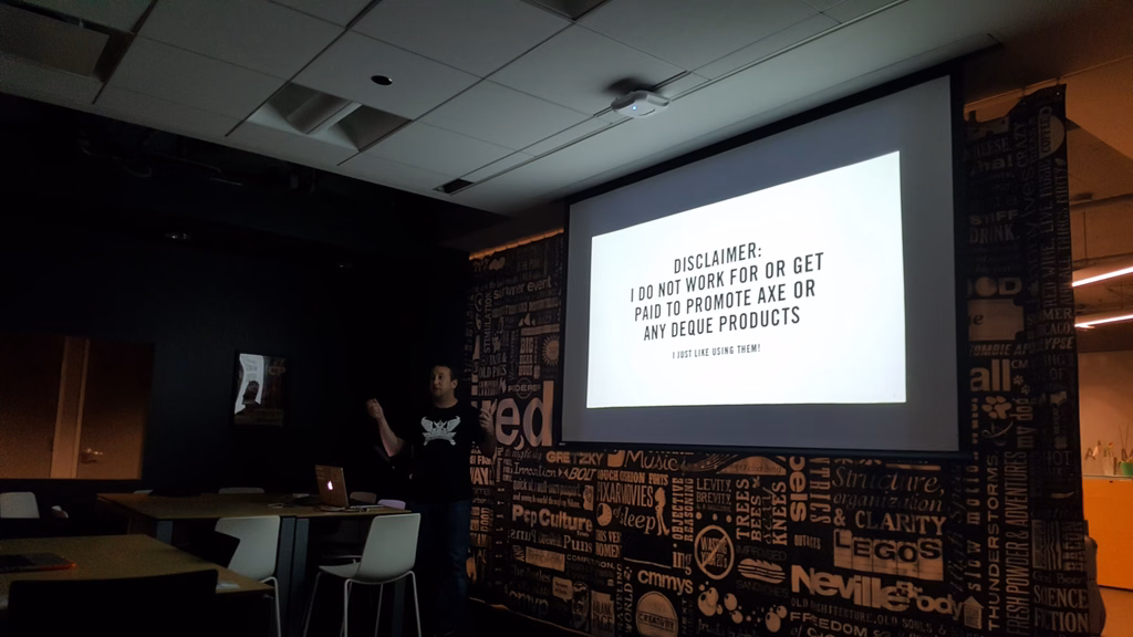 A dark room with a speaker presenting a slide of information with a stark white background and black text.